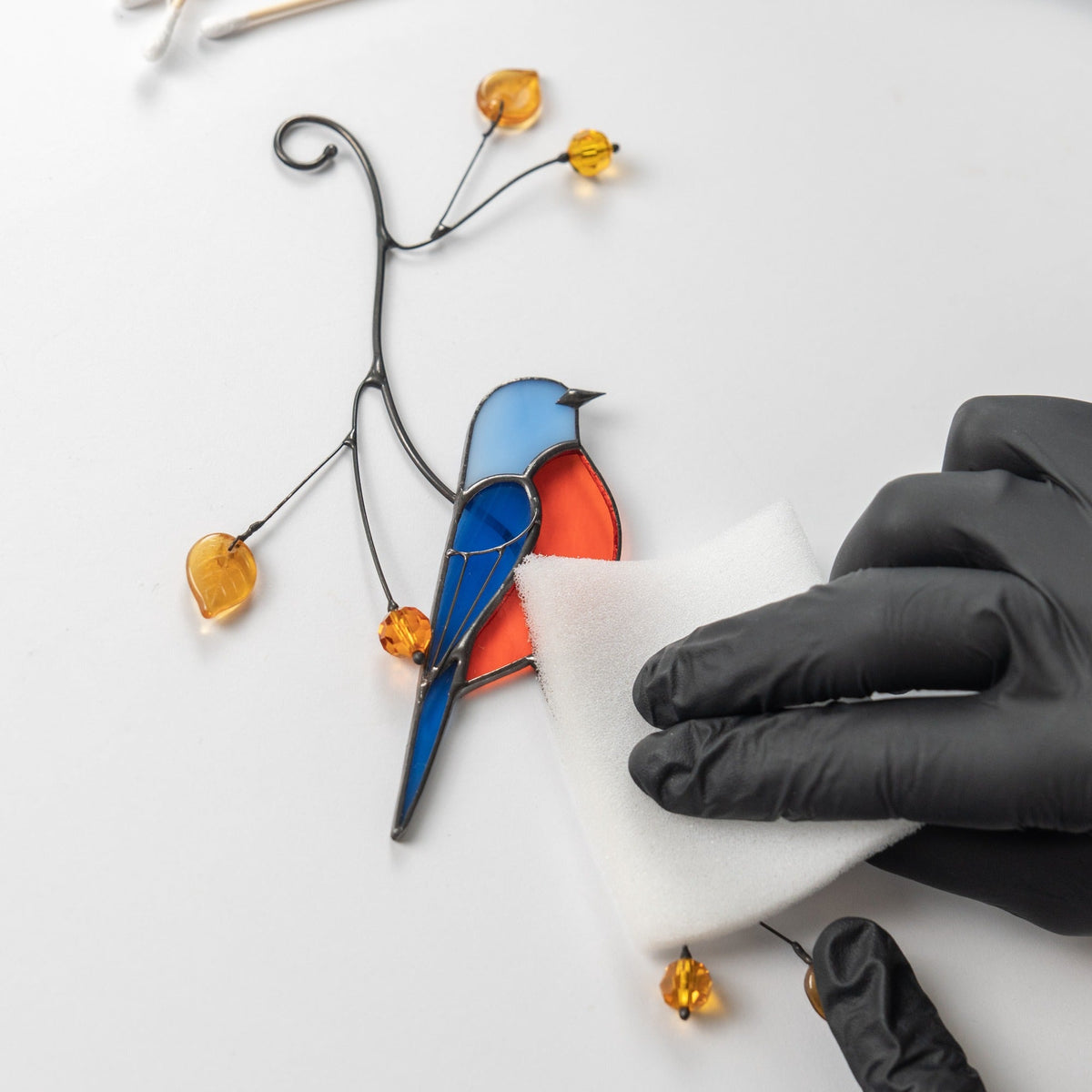 Stained glass bird sculpture with a hand wearing a black glove holding a small component.