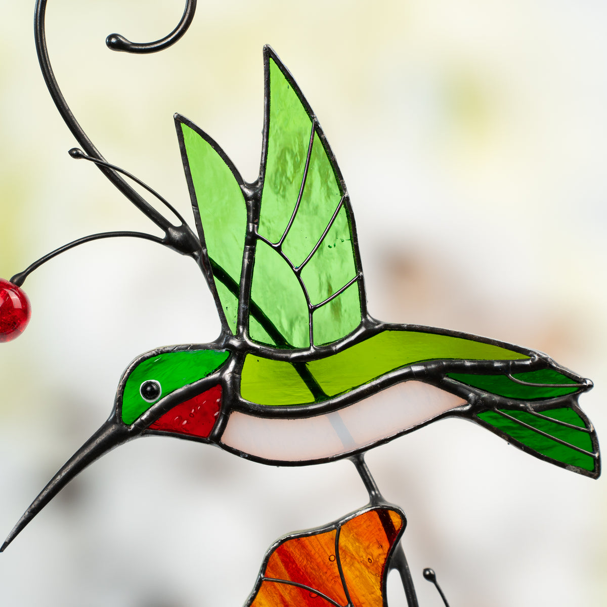 Close-up of green and red stained glass hummingbird in flight with detailed wing structure