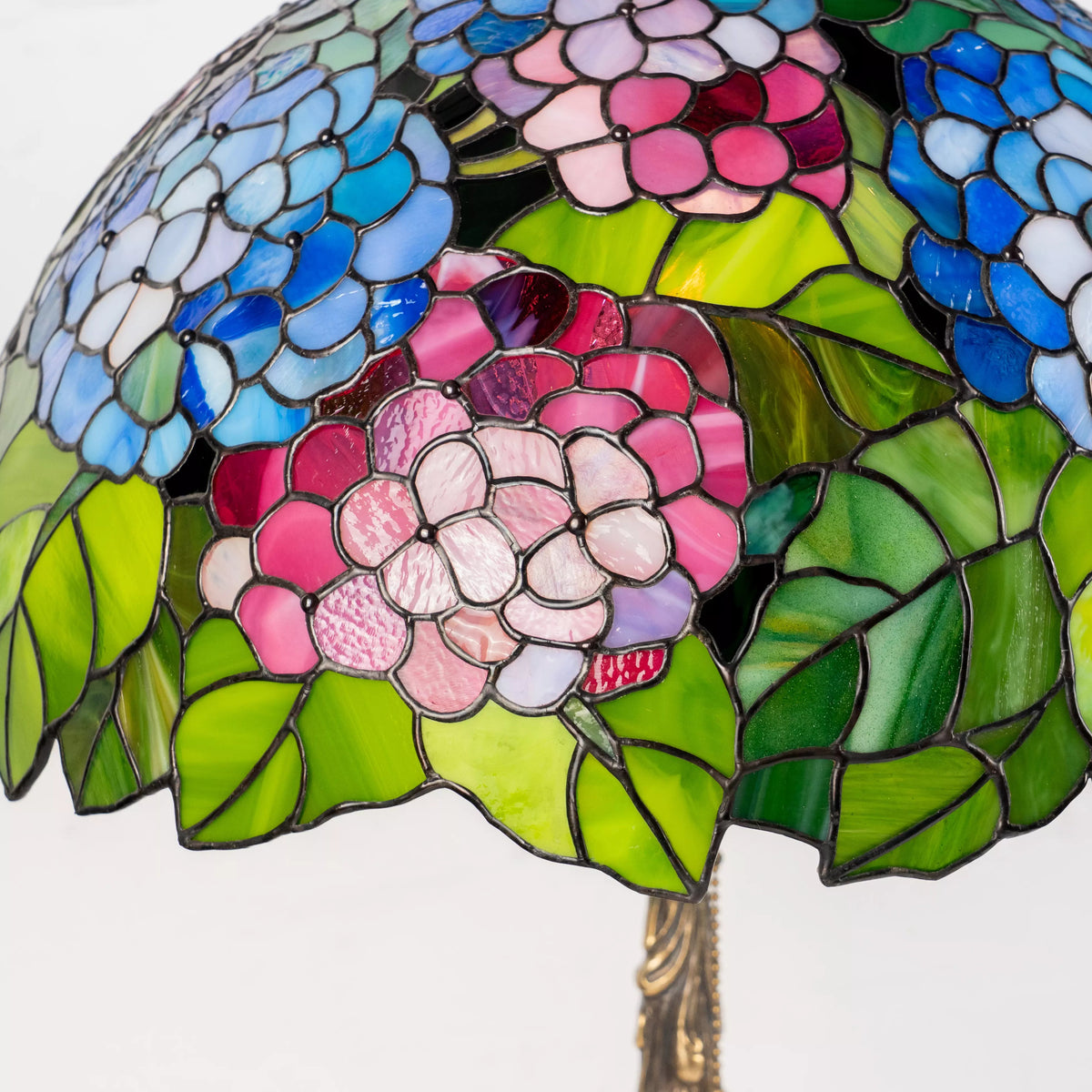 Detailed view of stained glass hydrangea flowers in pink with lush green leaves.