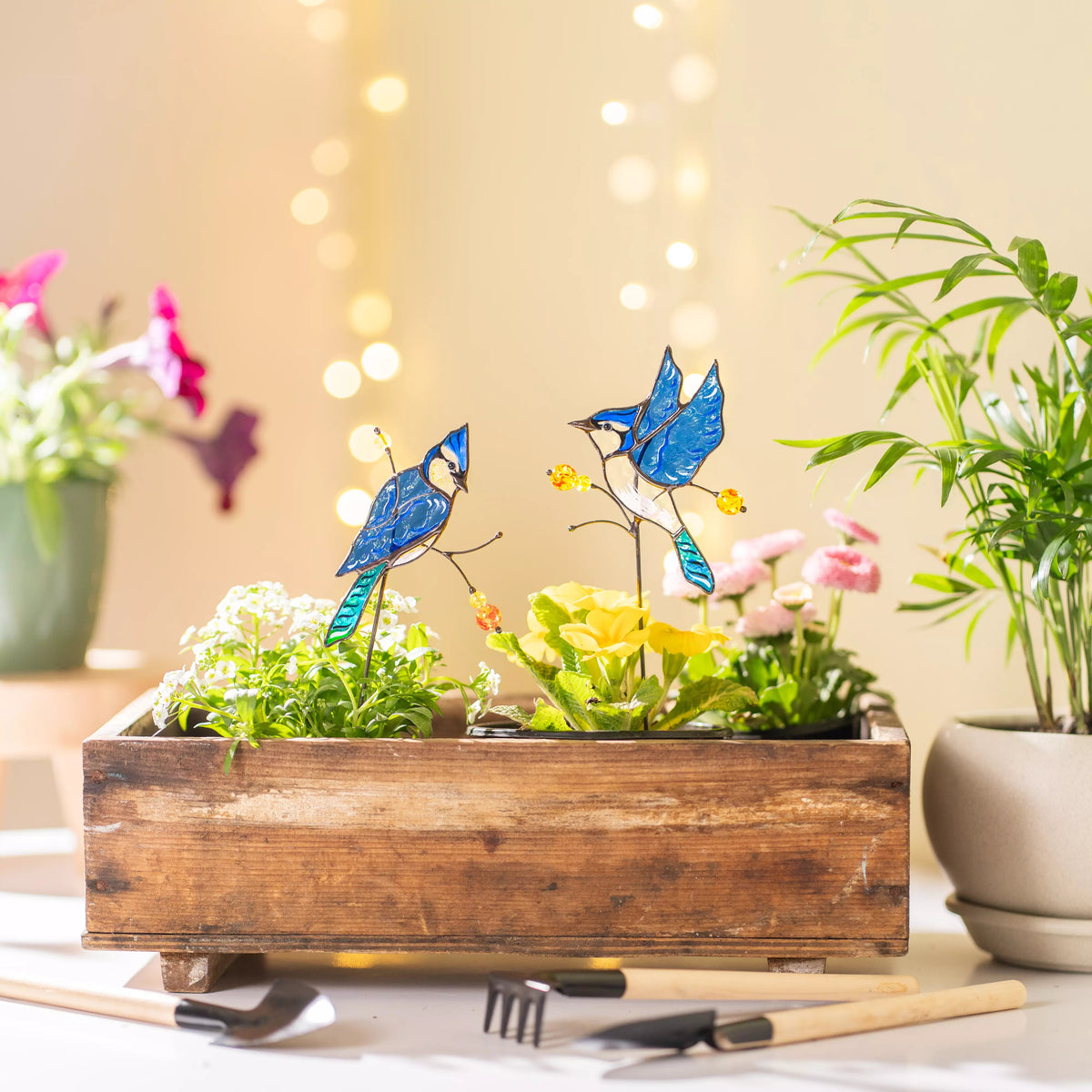 Garden scene with wooden planter, flowers, and glass bird plamnt stakes on a blurred background.