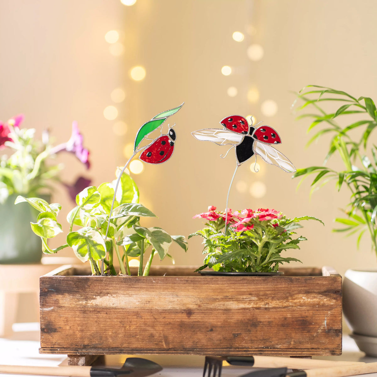 Stained galss ladybug and leaf plant stakes on a wooden planter with blurred lights in the background