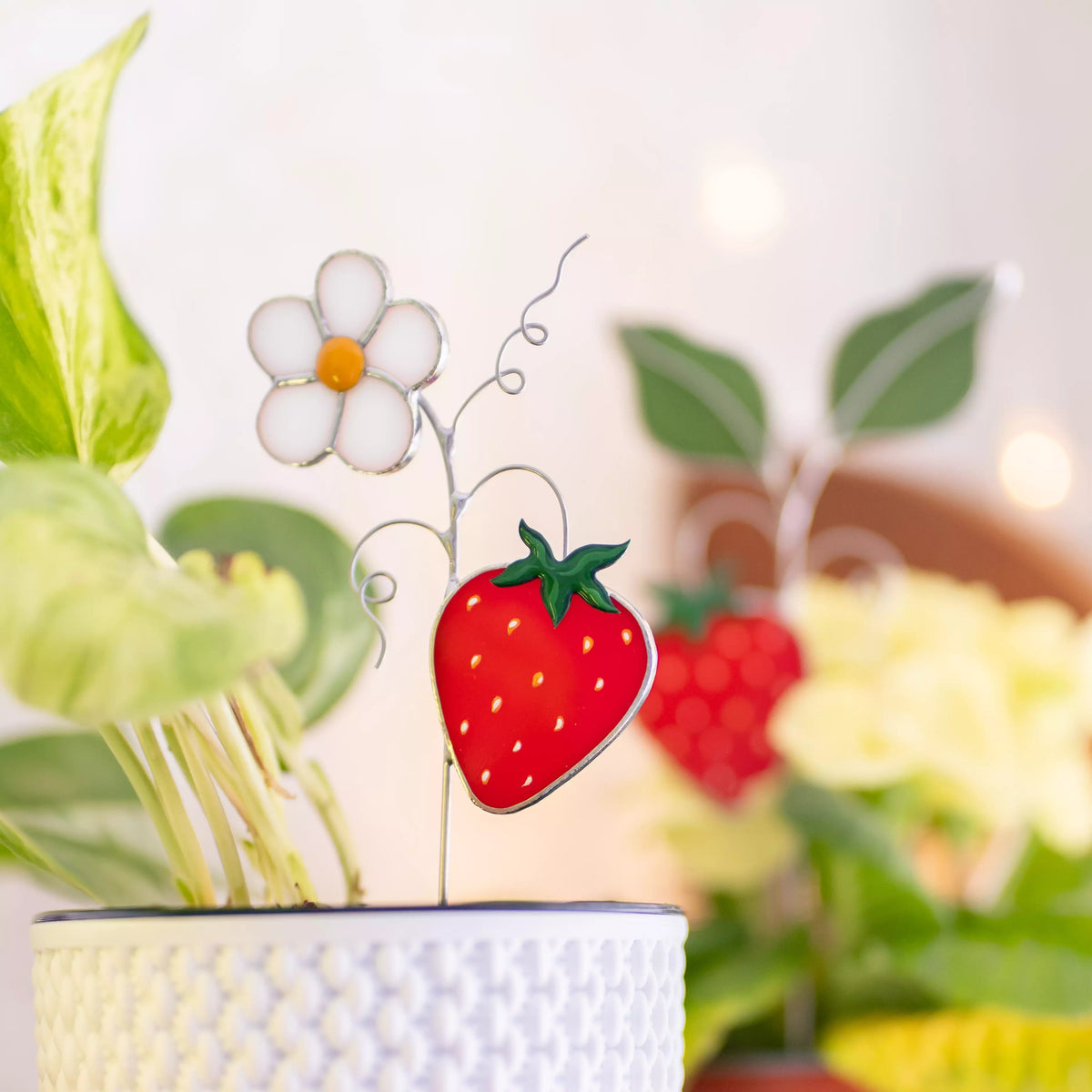 Stained glass plant stake strawberry and daisy ornament in a pot with blurred floral background