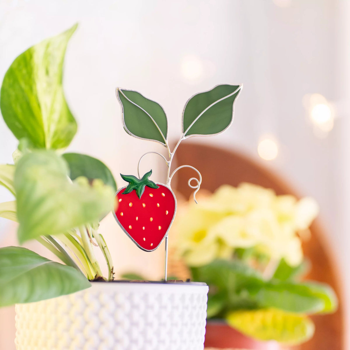 Stained glass strawberry plant stake with a blurred indoor setting