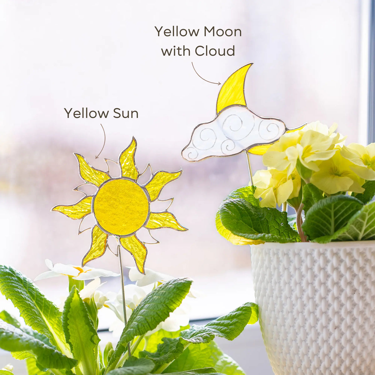 Variation of stained glass sun and moon plant stakes with text labels next to a potted plant.