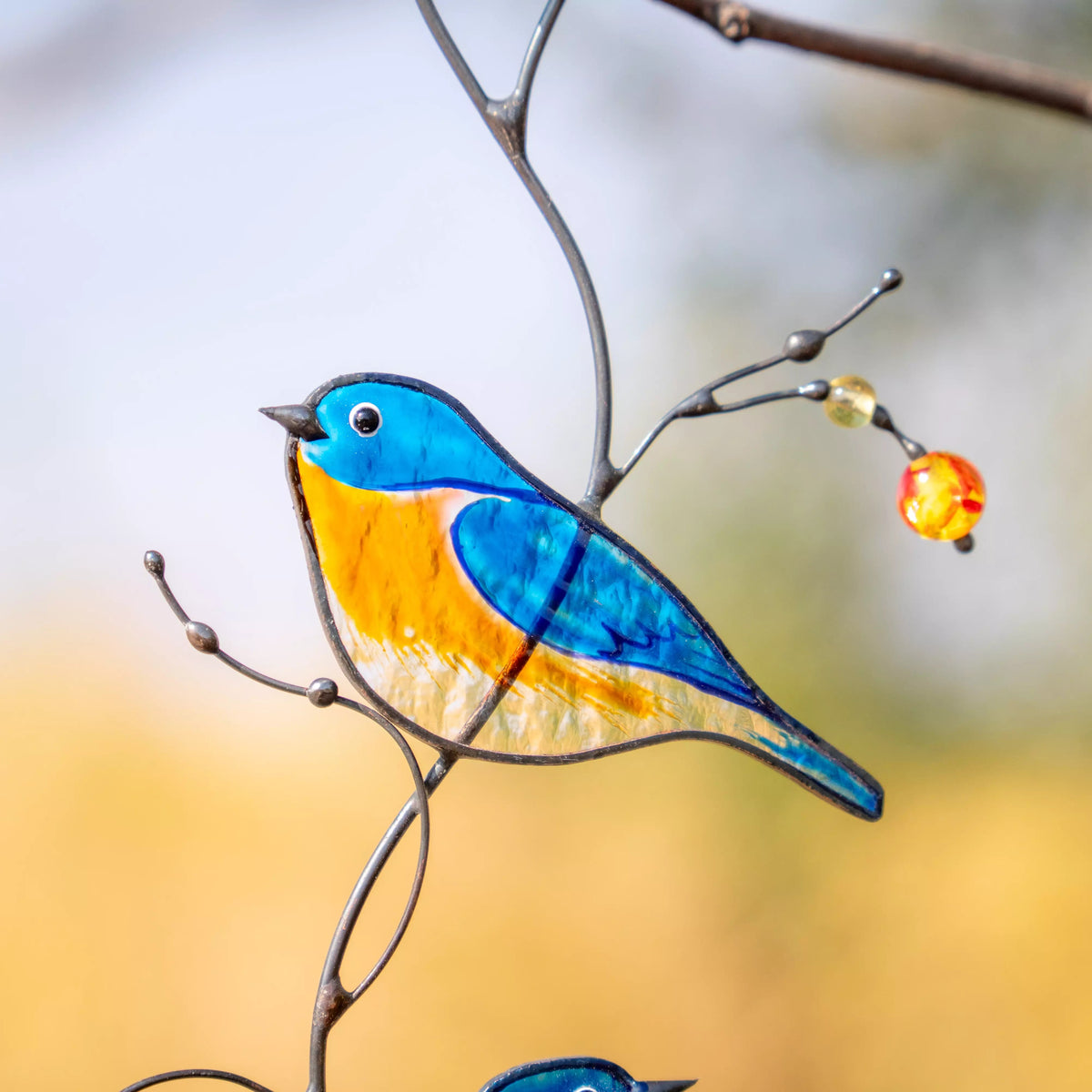 Stained glass bluebird ornament on a branch with a blurred background