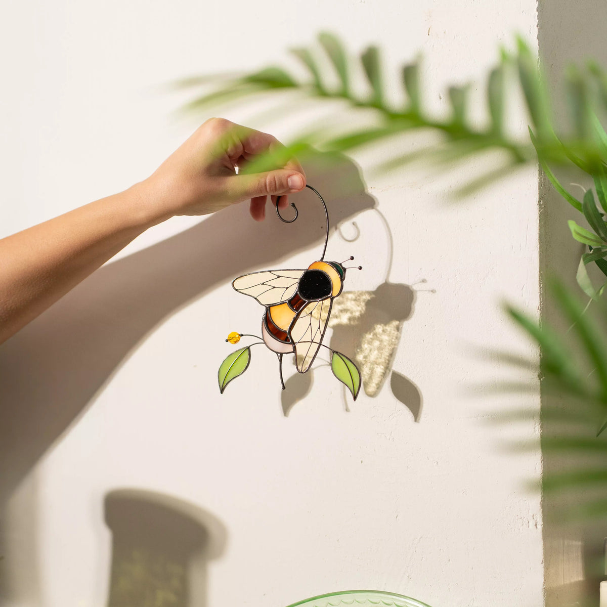 Hand holding a stained glass suncatcher bumble bee window hanging with leaves against a light background