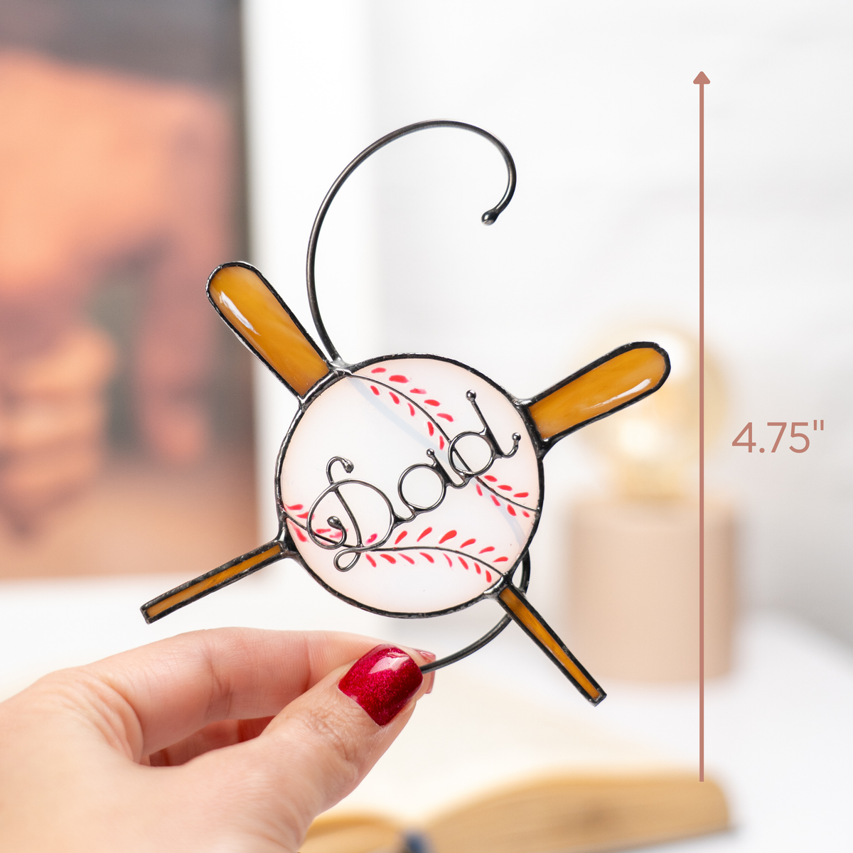 Hand holding glass ornament shaped as baseball with red stitches and brown bats