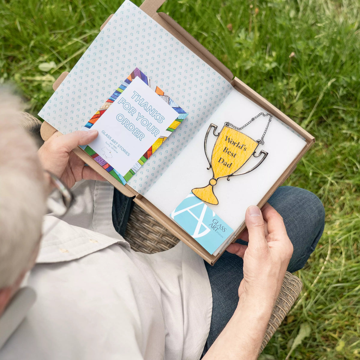 Person holding a box with stained glass, including a card and a small notebook, outdoors on grass.