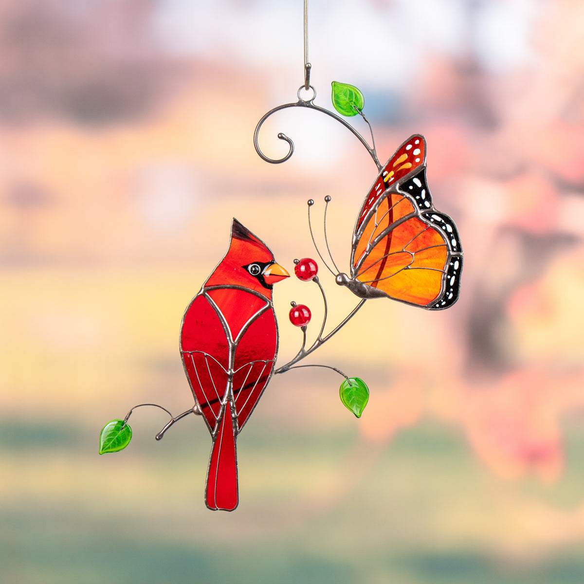 Cardinal and monarch butterfly stained glass suncatcher displayed outdoors with green garden background.