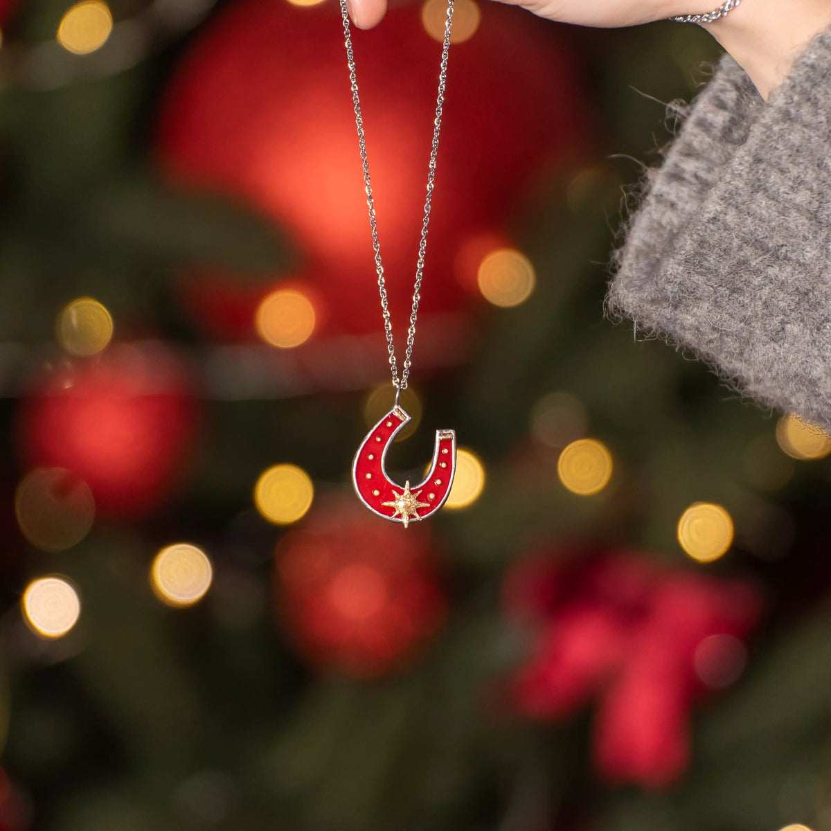 Horseshoe stained glass necklace held by a hand with a Christmas tree in the background