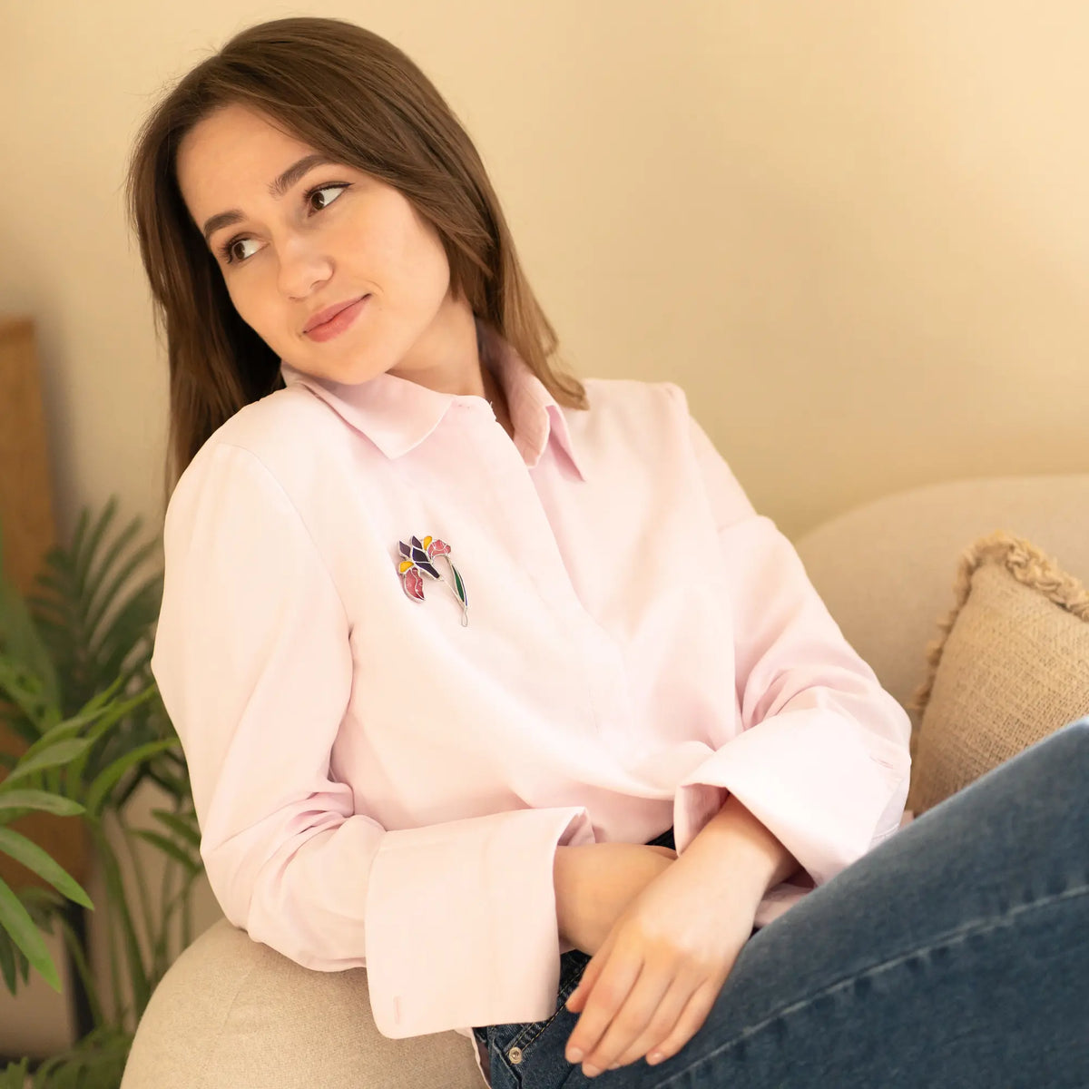 Woman wearing a light pink shirt with a colorful design, sitting on a couch.