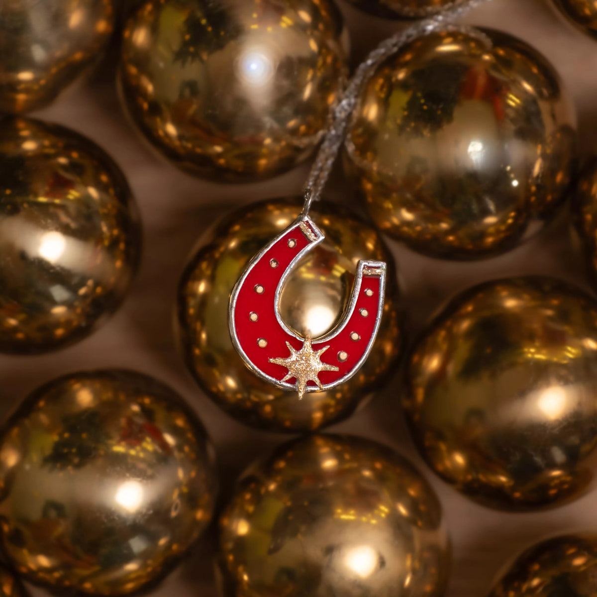 Red horseshoe-shaped stained glass pendant with a star on gold Christmas balls