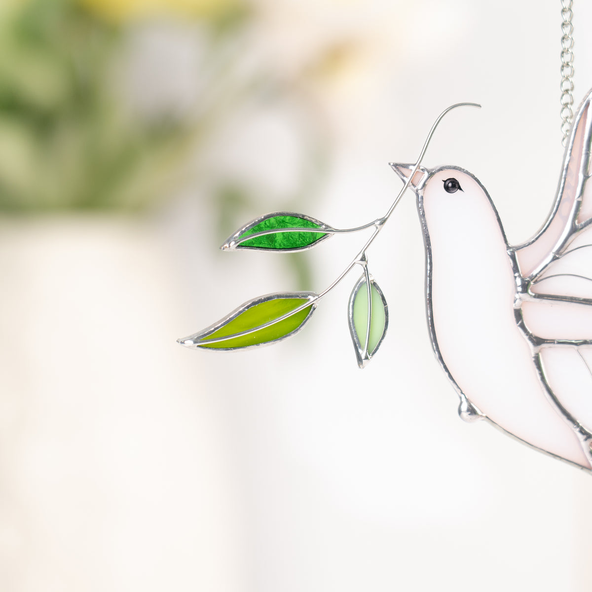 White stained glass dove with green leaves against a blurred background