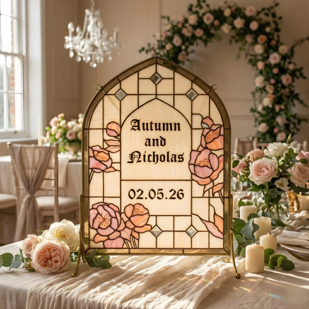 A personalized stained glass panel for "Autumn and Nicholas" with pink roses and a gold frame, placed on a decorated wedding reception table.