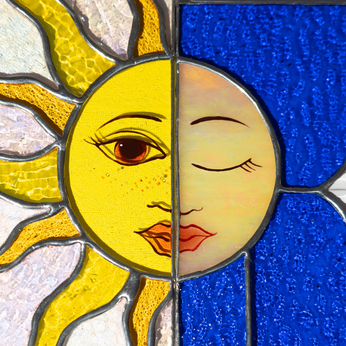 Close-up view of stained glass panel with a sun and moon face design.