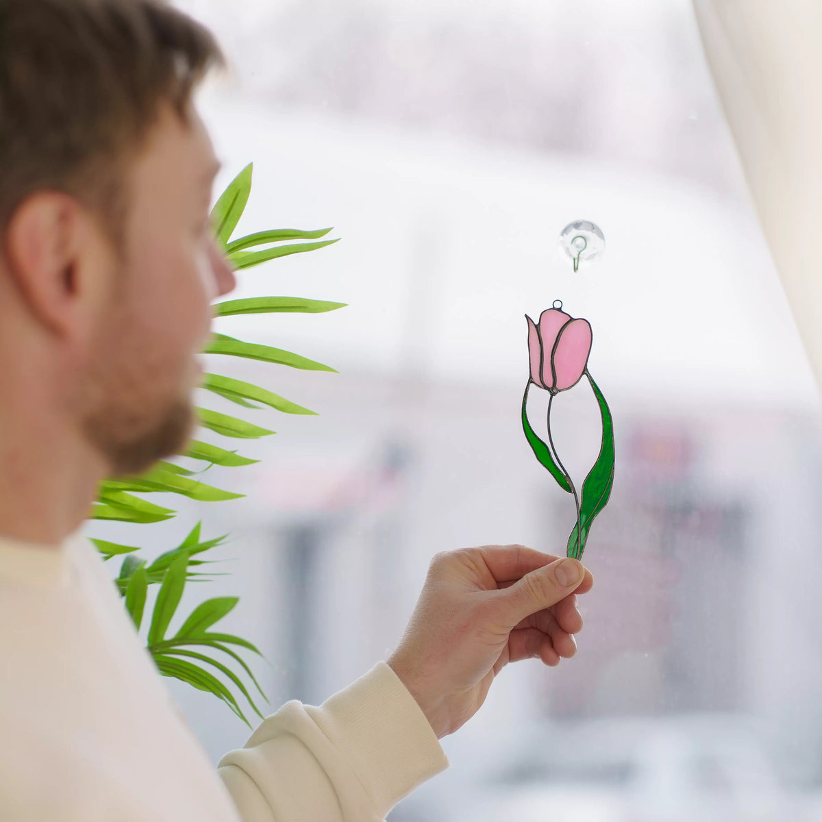 Person holding a pink tulip stained glass window sticker hanging with a blurred indoor background