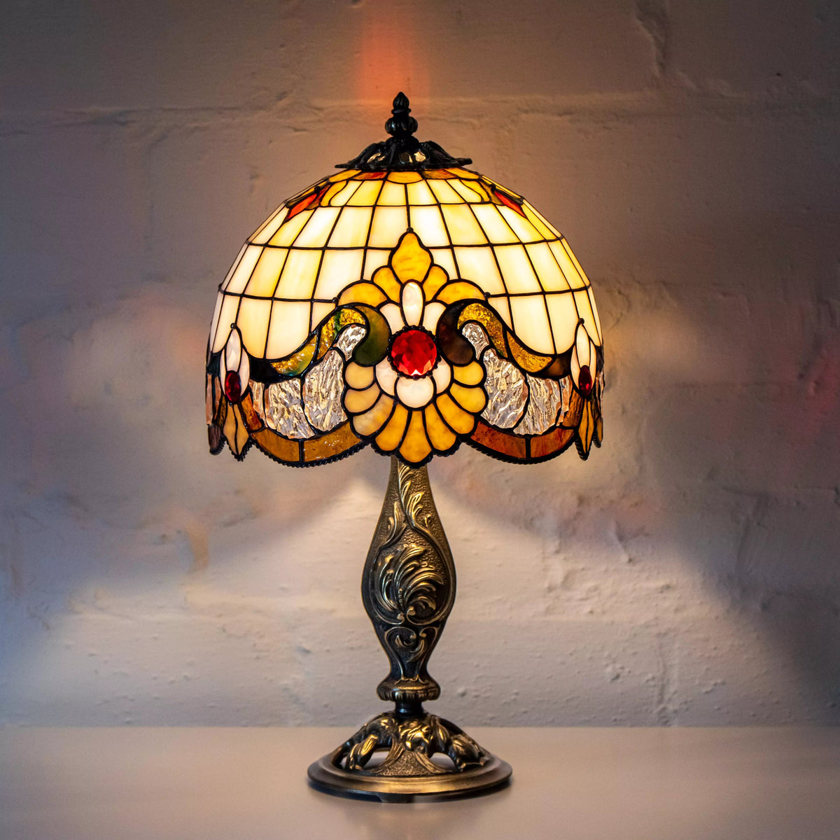 Lit stained glass lamp casting warm light with red details and bronze base
