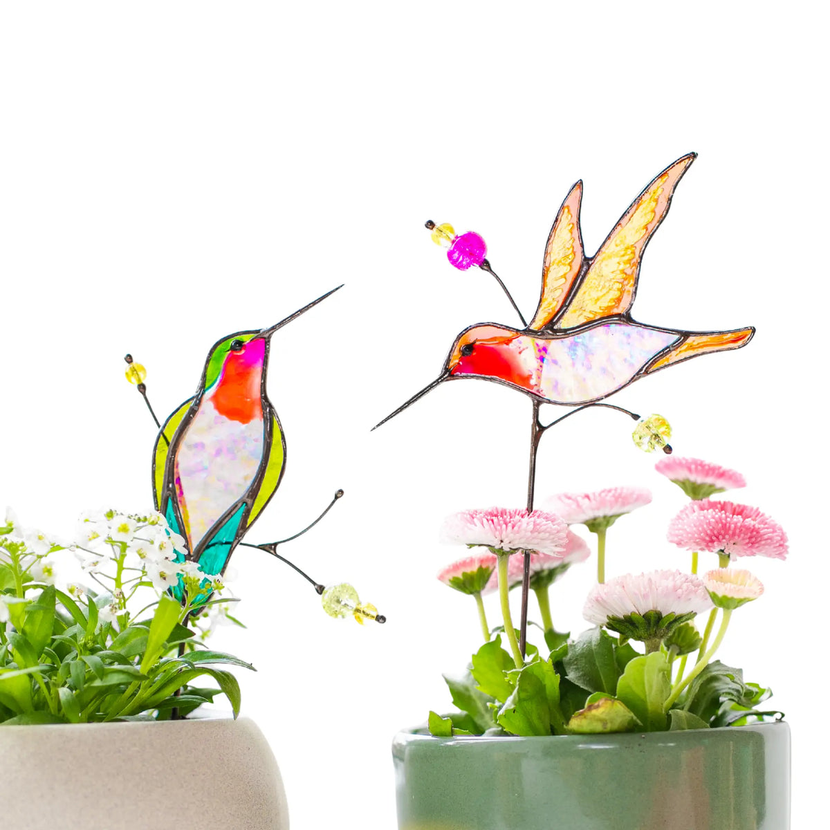 Two stained glass hummingbird plant stakes in flower pots on a white background