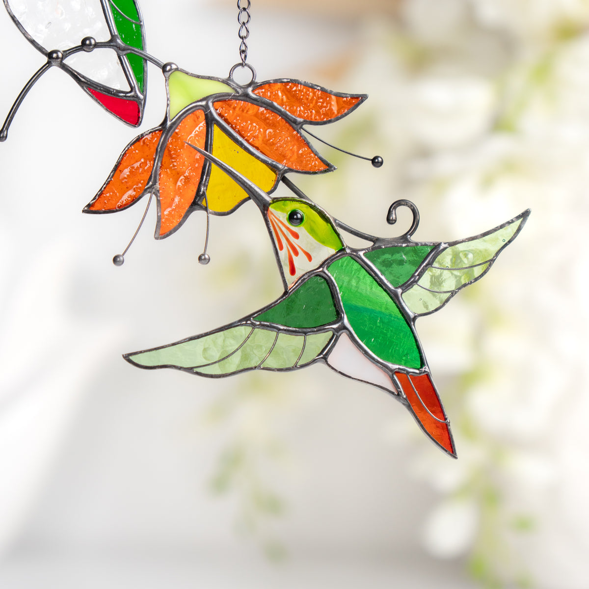 Lower hummingbird in stained glass art shown mid-flight with wings extended, sipping from flower.