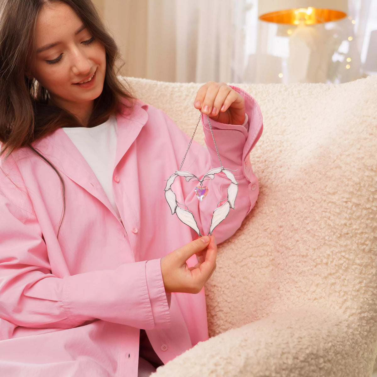 Lifestyle photo of a woman holding a winged heart stained glass suncatcher with white glass feathers and a crystal heart