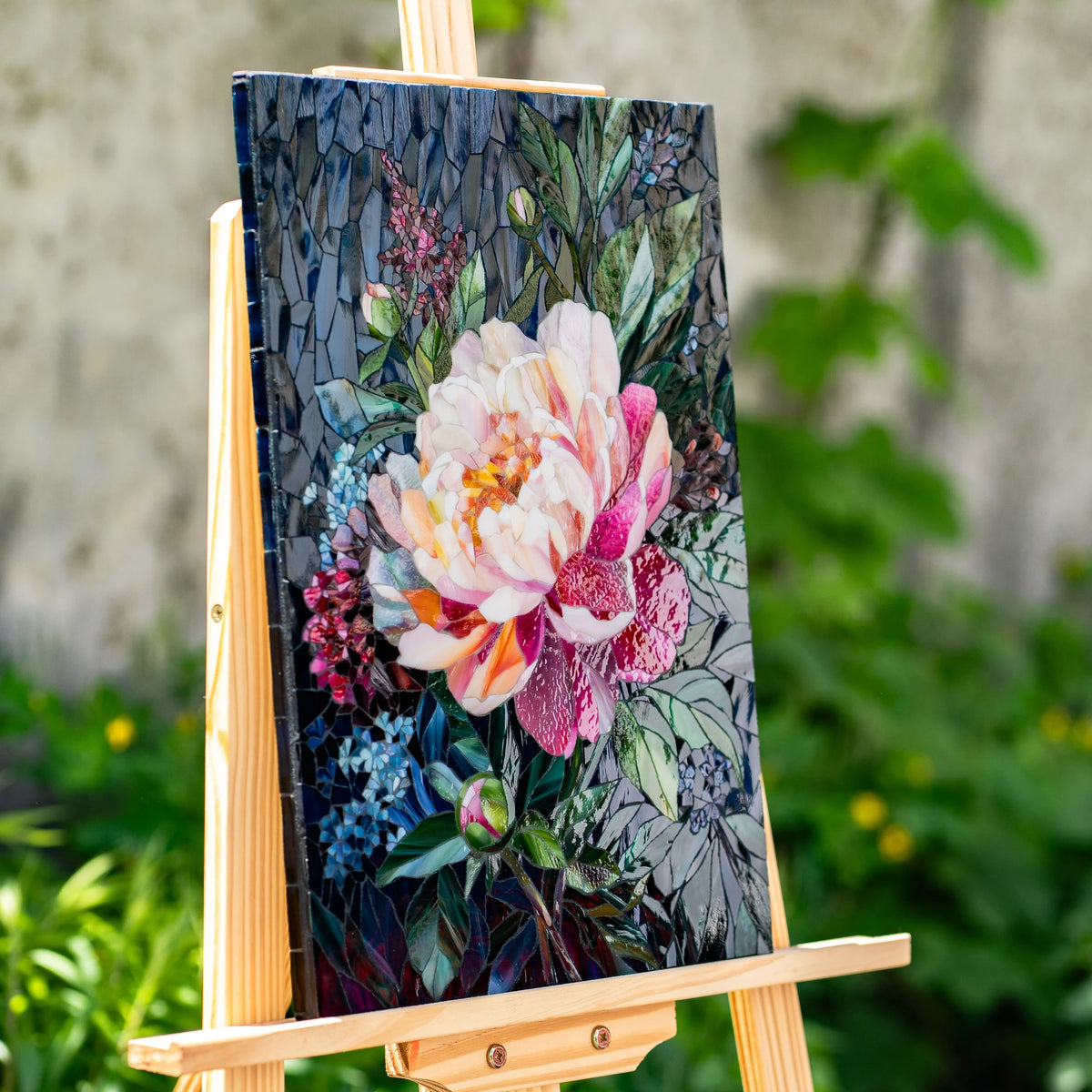 Angled view of a peony stained glass mosaic panel on an easel, revealing the depth and glossy texture of hand-cut cathedral glass on a navy background — handmade floral wall art