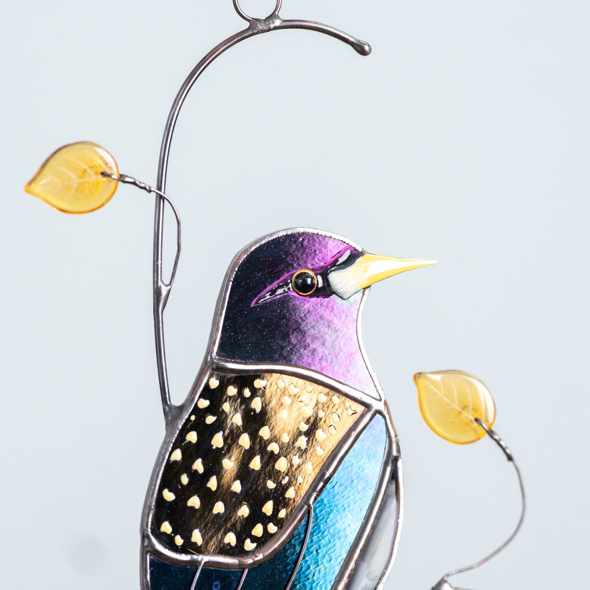Side view of robin glass suncatcher with warm-colored leaves, hanging with white background.