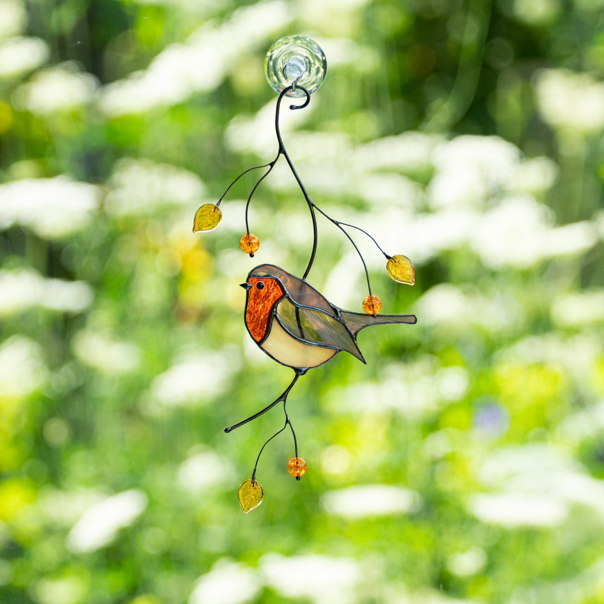 Full stained glass robin suncatcher hanging on window, decorated with yellow leaves and amber beads against a sunny garden.