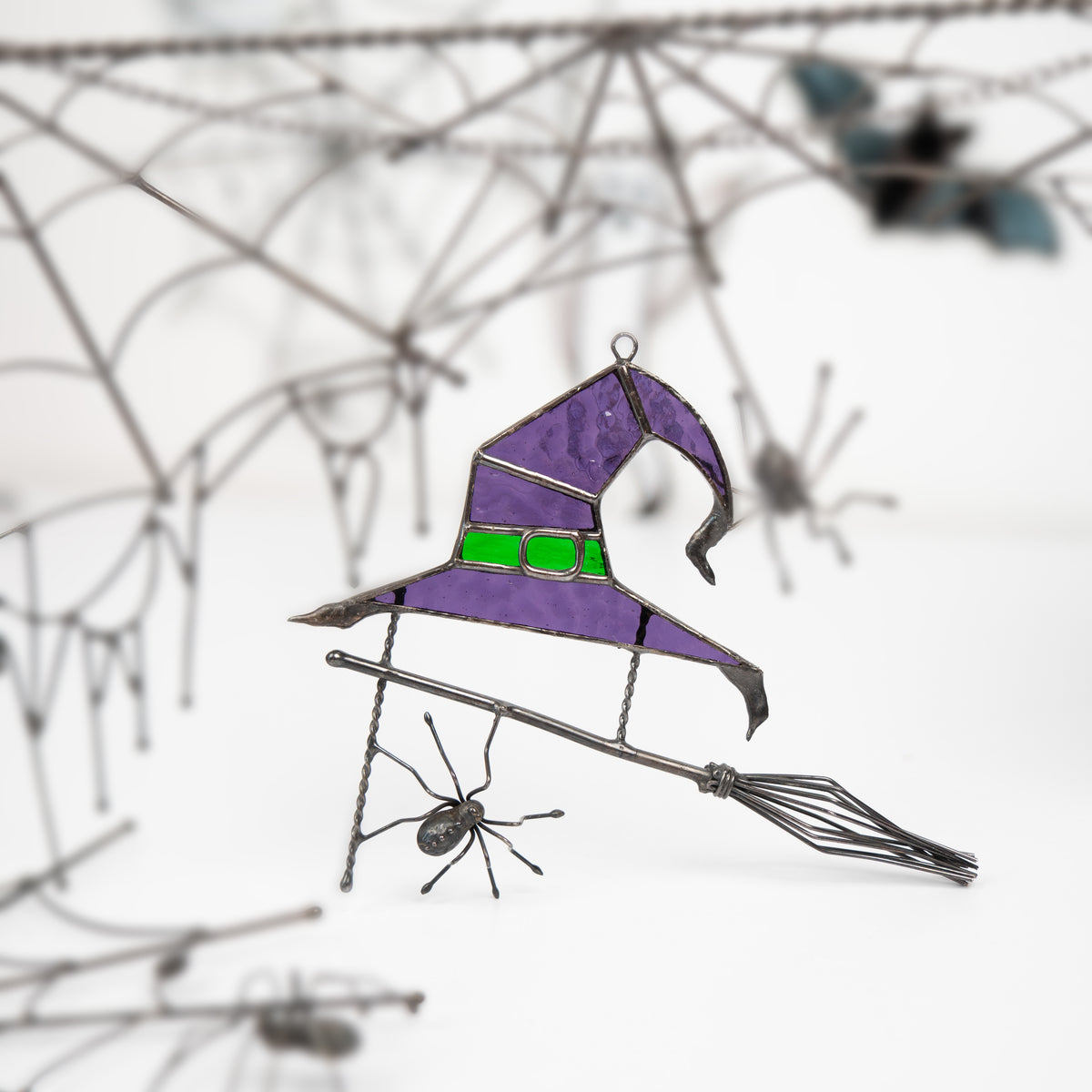 Witch hat made with stained glass, shown with ghostly Halloween signs and soft-focus decor in background.
