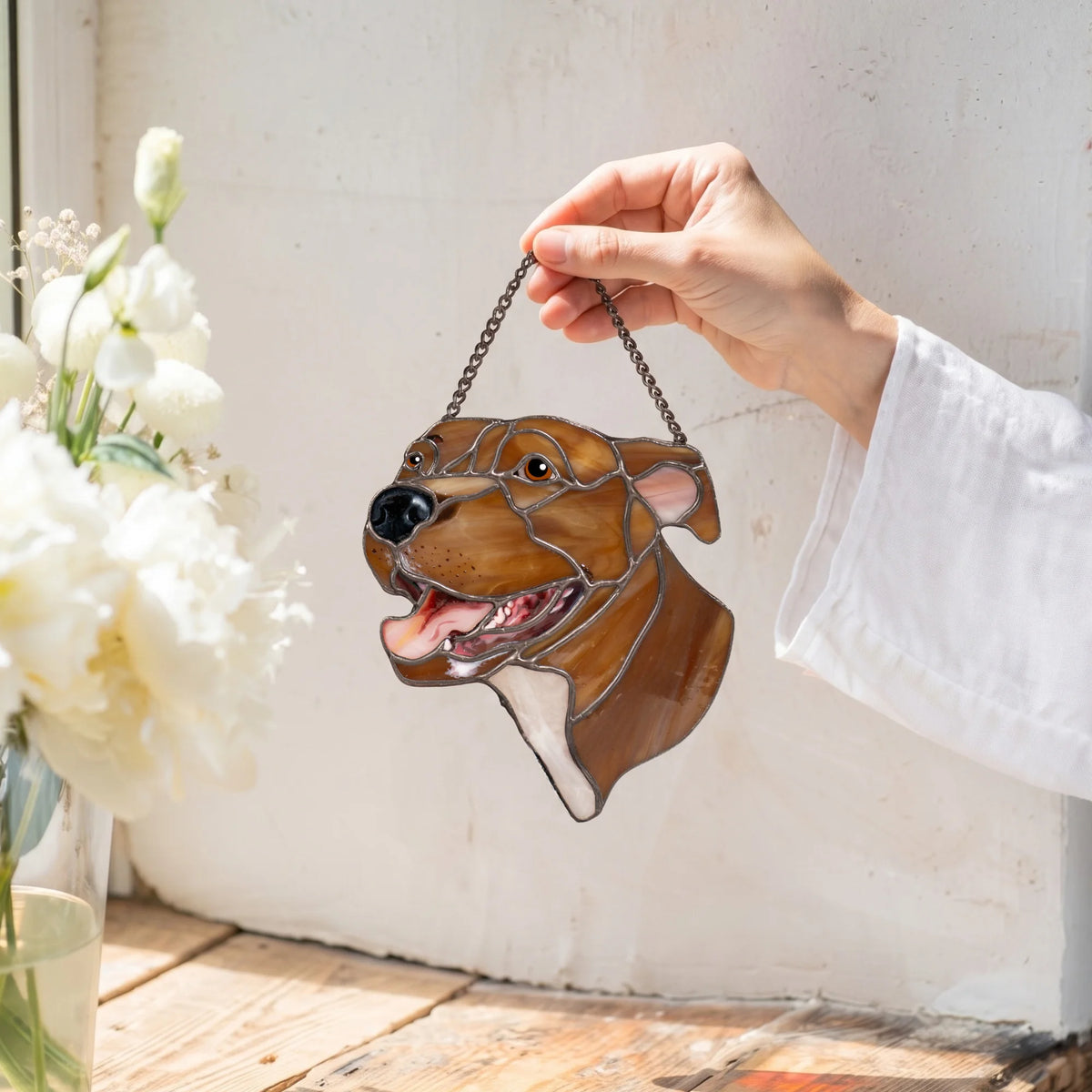 Custom pet suncatcher of a happy brown dog held up by its chain next to a vase of white peonies - a handmade Tiffany stained glass portrait from photo and a gentle memorial suncatcher for a beloved pet