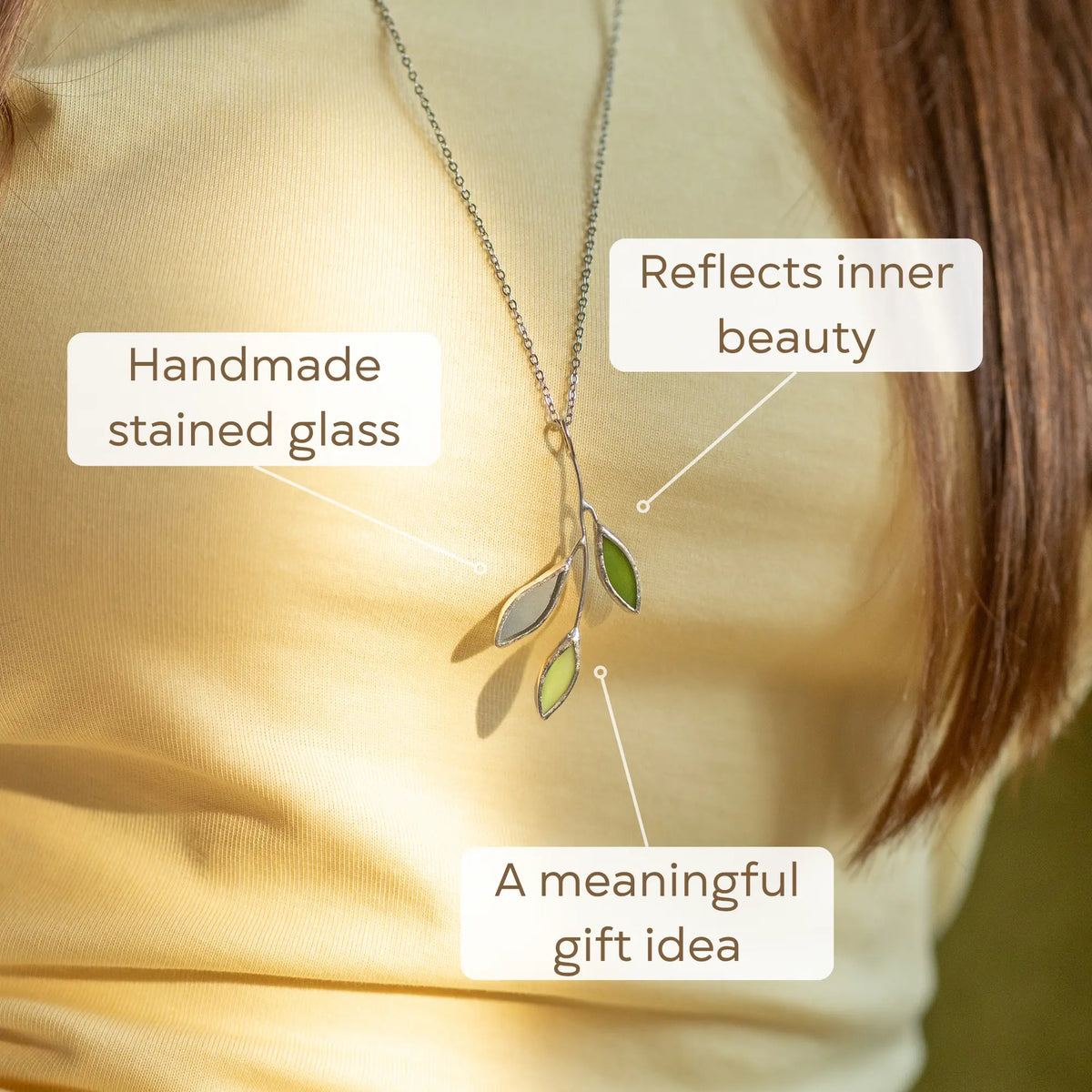 Close-up of the handmade stained glass sprig pendant - green and pale glass leaves on a slender silver branch, a nature-inspired botanical necklace and gift for plant lovers