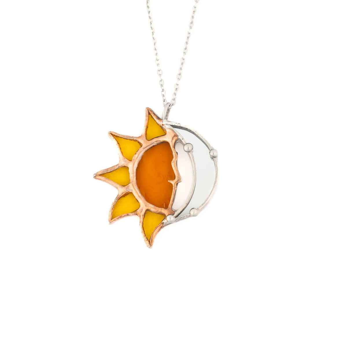 Handmade stained glass sun and moon necklace shown up close - a glowing amber glass sun with pointed rays beside a bright silver crescent moon, on a fine stainless steel chain