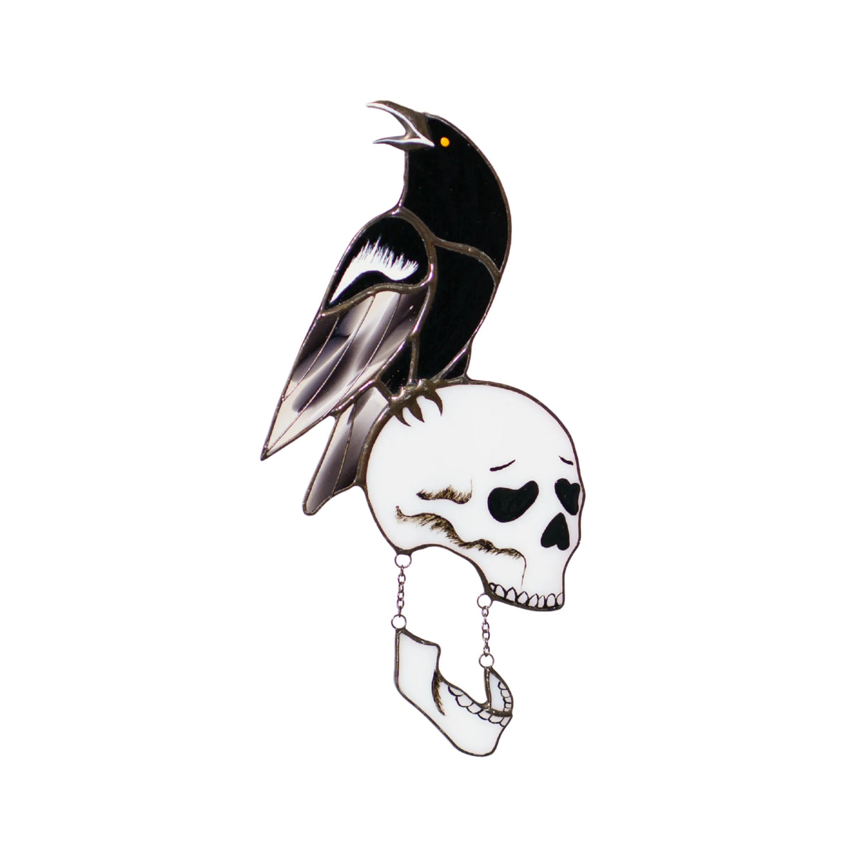 Handmade stained glass raven and skull suncatcher on a white background, a cawing black raven with an iridescent lilac wing perched on a bone-white skull whose hinged jaw hangs from delicate chains - gothic Halloween decor