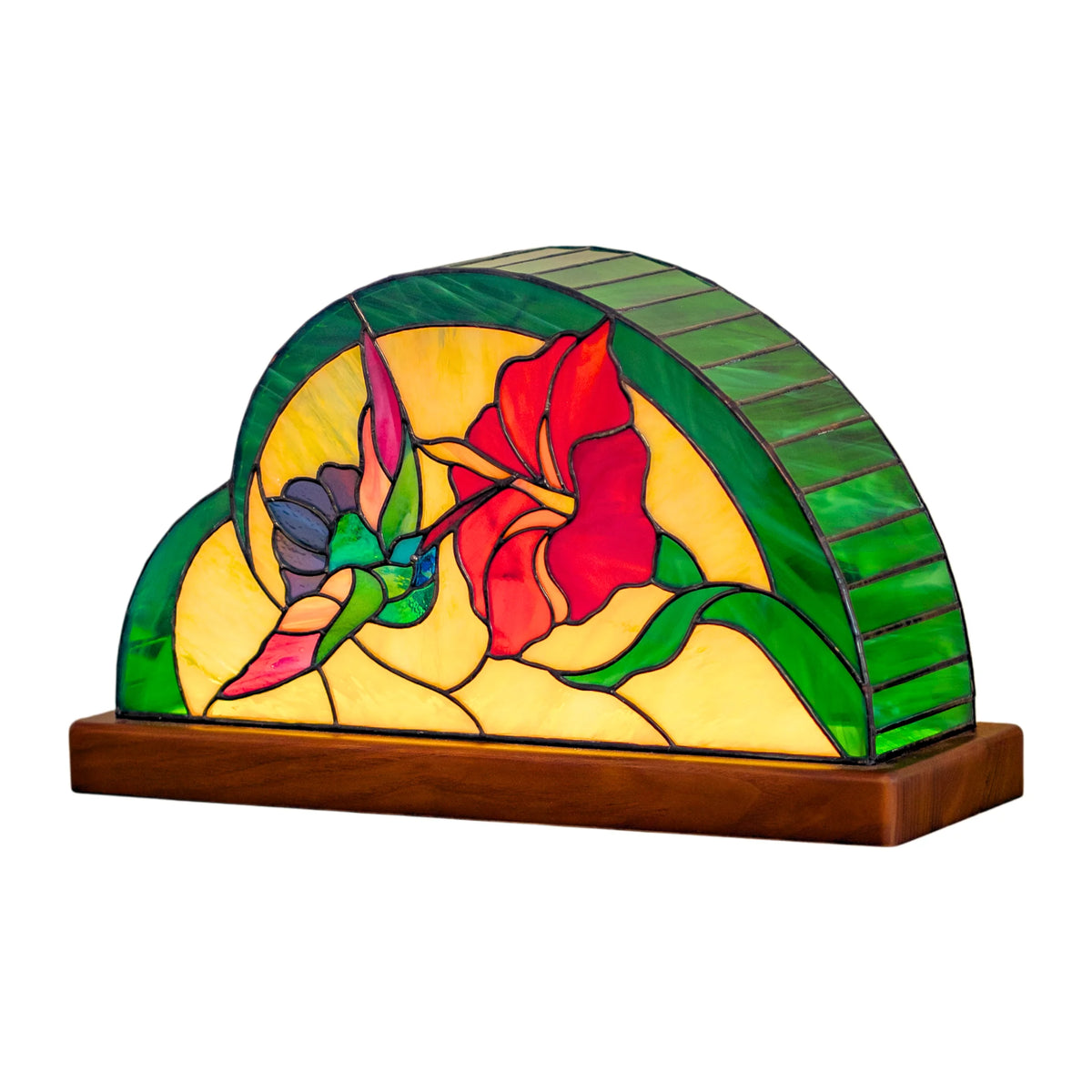 Handmade Tiffany-style stained glass table lamp on a wooden base showing a hummingbird sipping from a red hibiscus among green leaves - hand-cut stained glass home decor on a white background