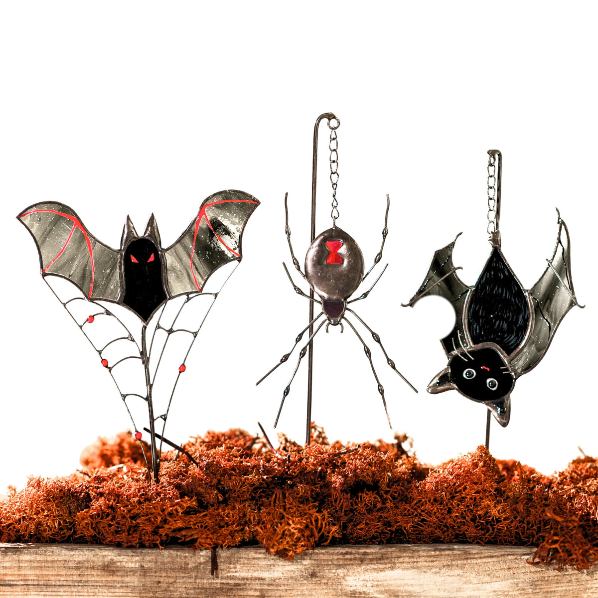 Set of three Halloween stained glass plant stakes on a white background - vampire bat on a beaded wire web, black widow spider and an upside-down cat-bat with green eyes