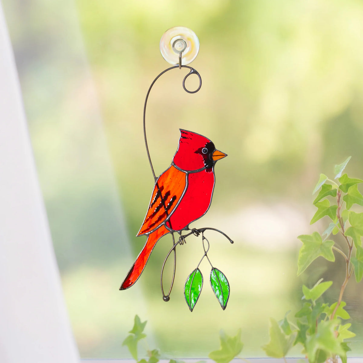 Red cardinal stained glass suncatcher on a bright window with a suction cup and green garden beyond, red cardinal on a wire branch with leaves - handmade memorial bird suncatcher