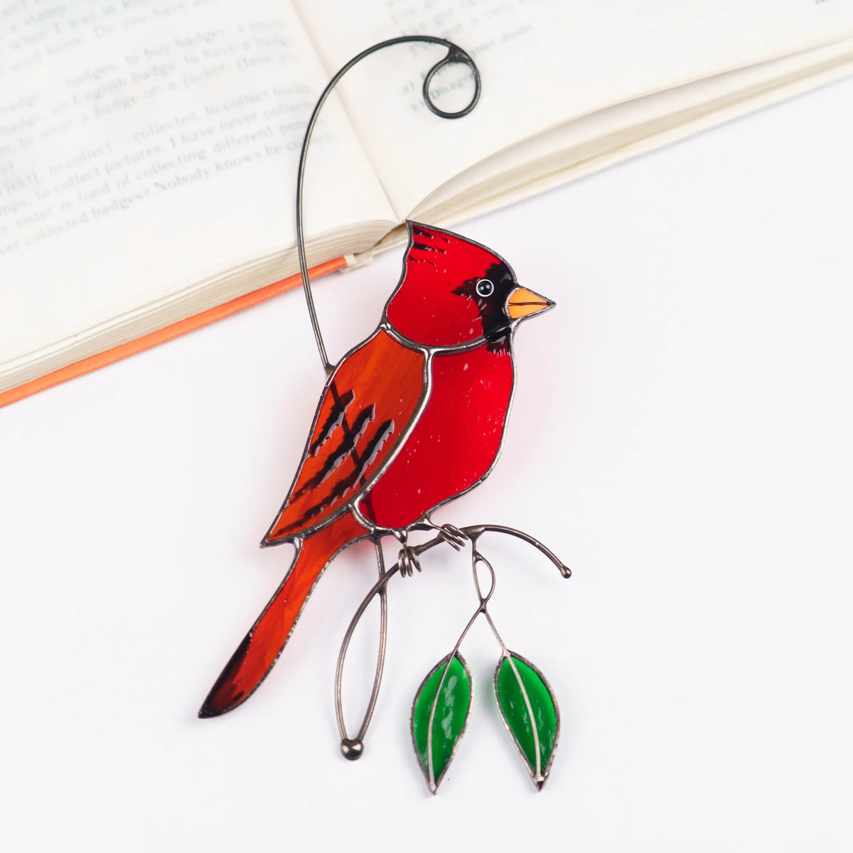 Stained glass red cardinal suncatcher resting on an open book, red cardinal with an orange wing on a wire branch with green leaves - handmade bird suncatcher and memorial keepsake for readers