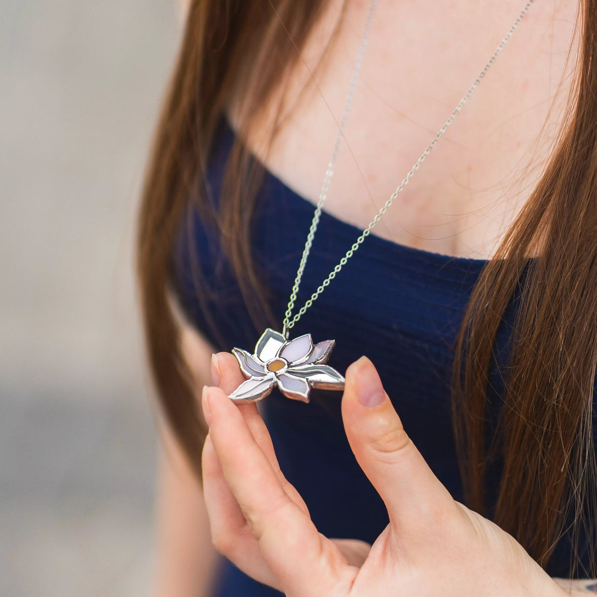 Woman holding the White Lotus stained glass pendant against a navy top, showing the white glass petals and amber center - handmade lotus necklace symbolizing purity and calm