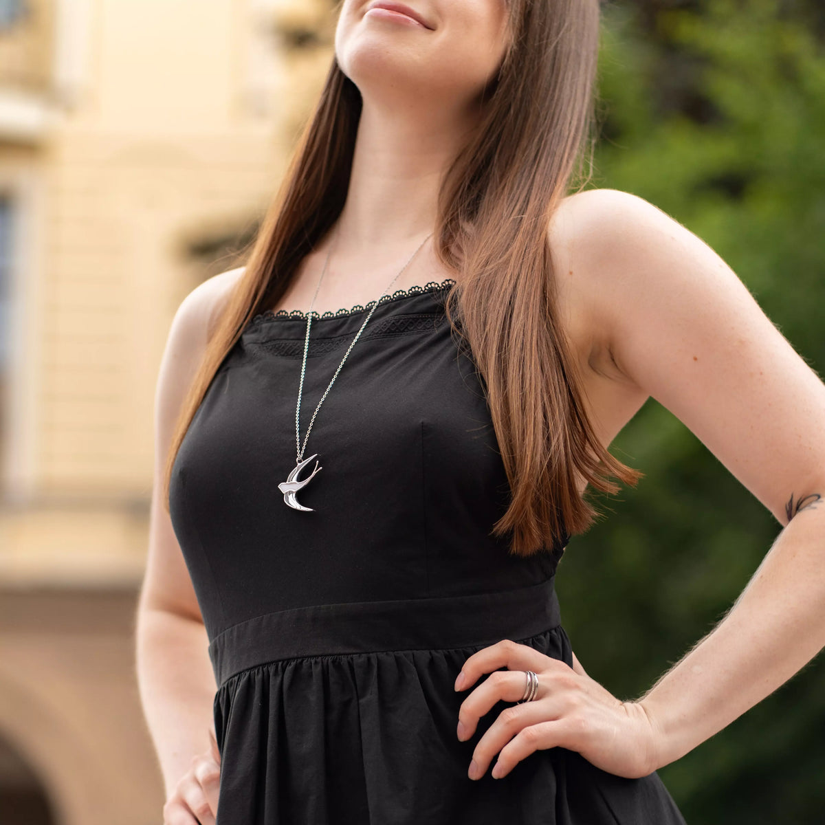 White Swallow stained glass necklace worn with a black dress outdoors, the silver-and-white bird pendant on a long chain - handmade stained glass bird jewelry and a gift for her