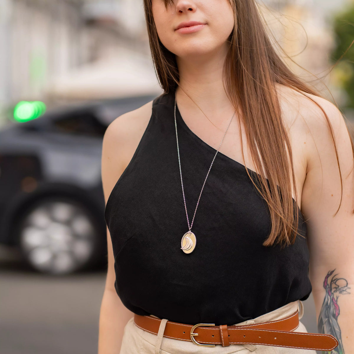 Woman in a black one-shoulder top wearing the stained glass moon necklace on a long silver chain, the iridescent crescent moon pendant resting at her waist - handmade celestial jewelry for everyday wear