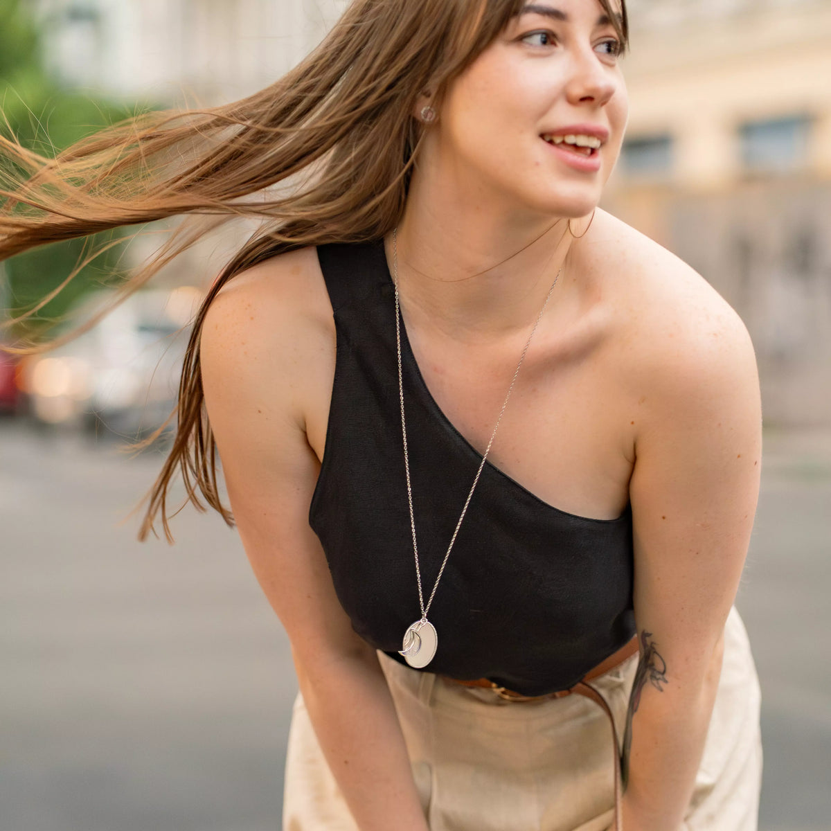 Smiling woman with hair blowing in the wind wearing a handmade stained glass moon necklace on a long chain - the iridescent crescent moon and mirror pendant catching the light, celestial jewelry gift