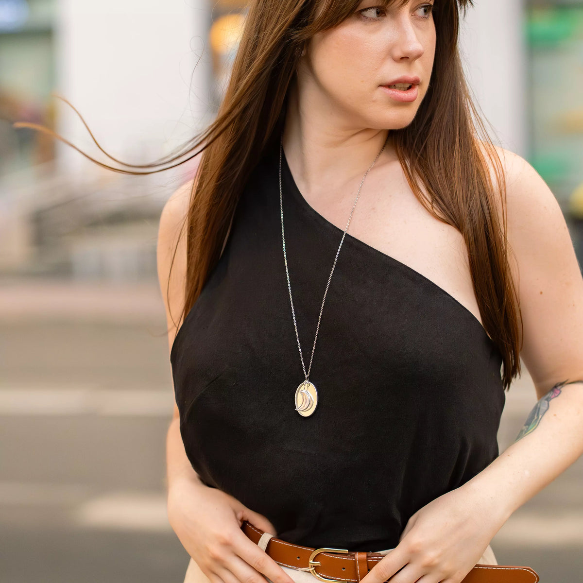 Woman in a black top and cognac leather belt wearing the stained glass moon necklace on a long silver chain, the iridescent crescent moon pendant at her midriff - handmade celestial gift for her