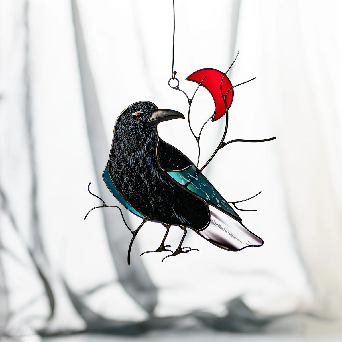 Handmade stained glass raven and red crescent moon suncatcher against soft grey drapery, glossy black raven with a teal iridescent wing perched on wire branches - gothic and celestial window art