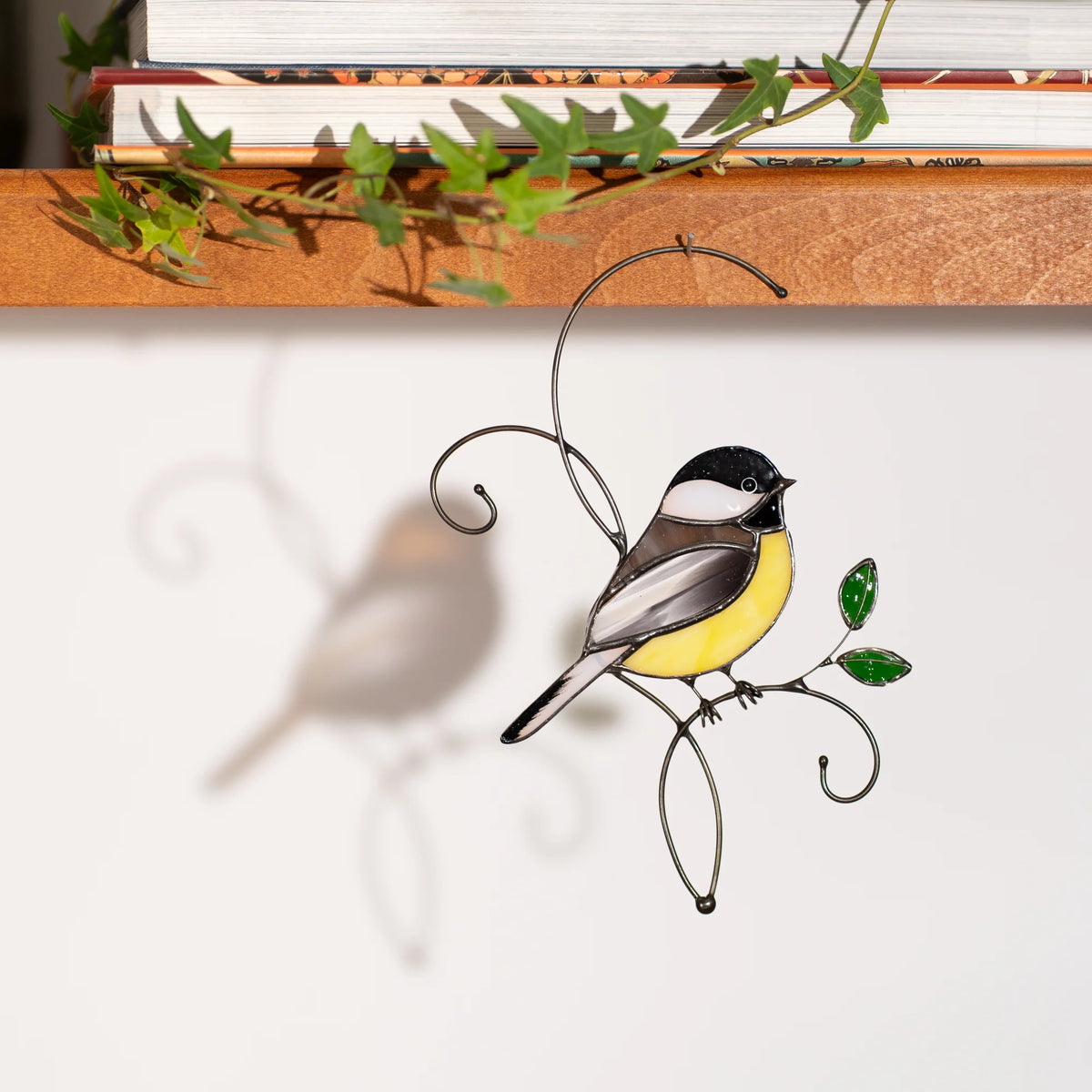 Stained glass chickadee suncatcher hanging below the shelf , black-capped chickadee with a yellow belly on a wire branch with green leaves - handmade bird gift