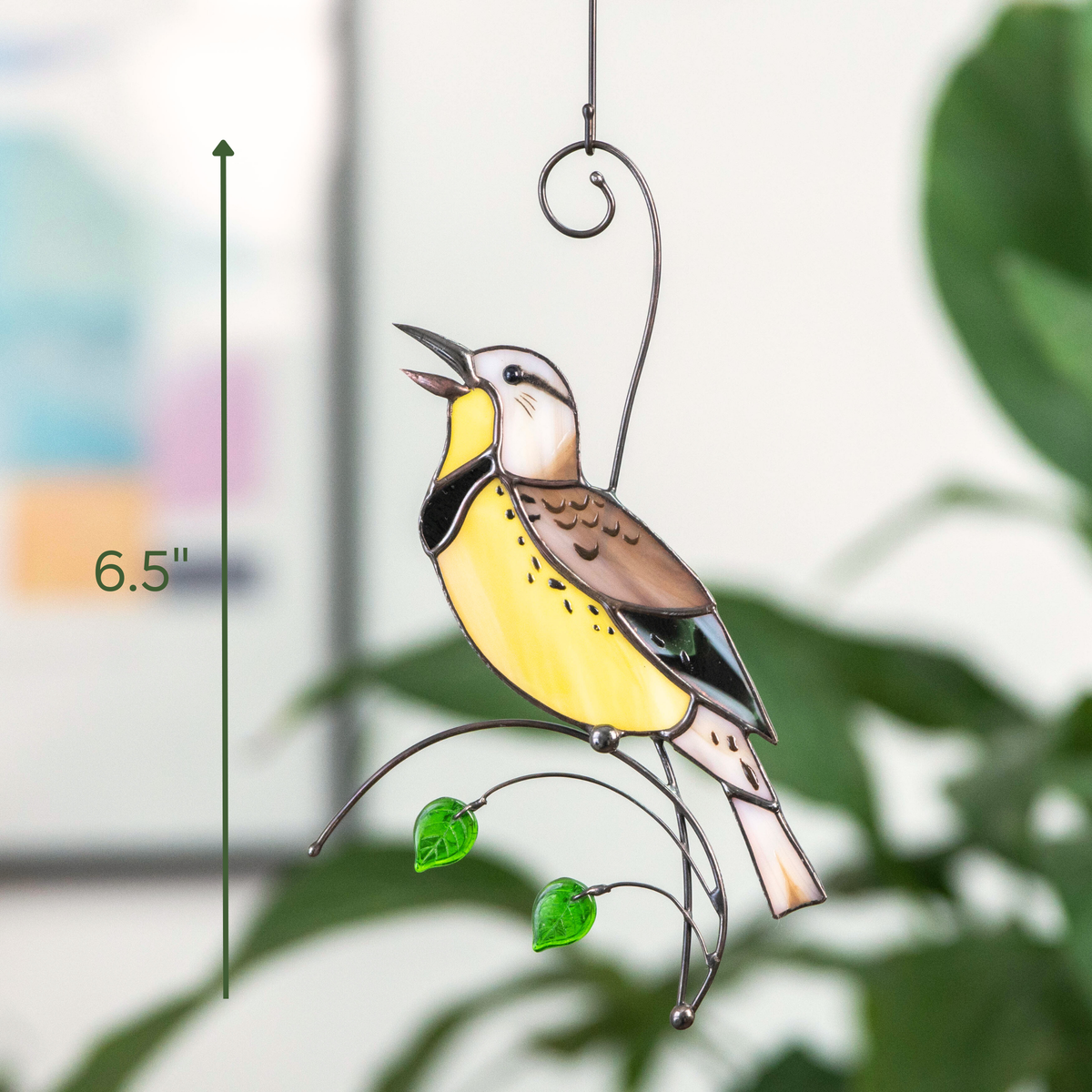 Yellow meadowlark suncatcher measured at 6.5 inches hanging in front of houseplants
