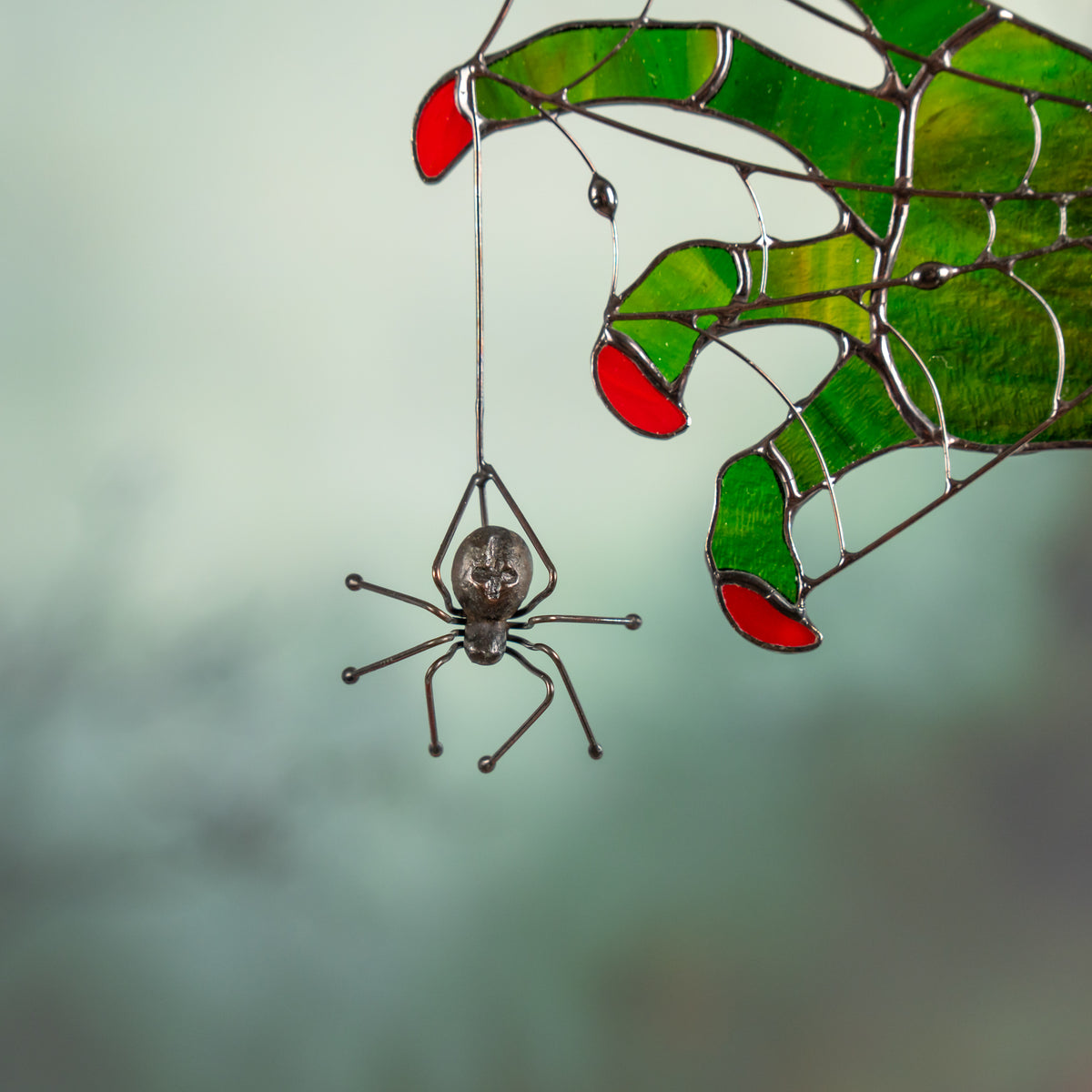 Zoomed-in photo of metal spider hanging from stained glass witch fingers with red tips.