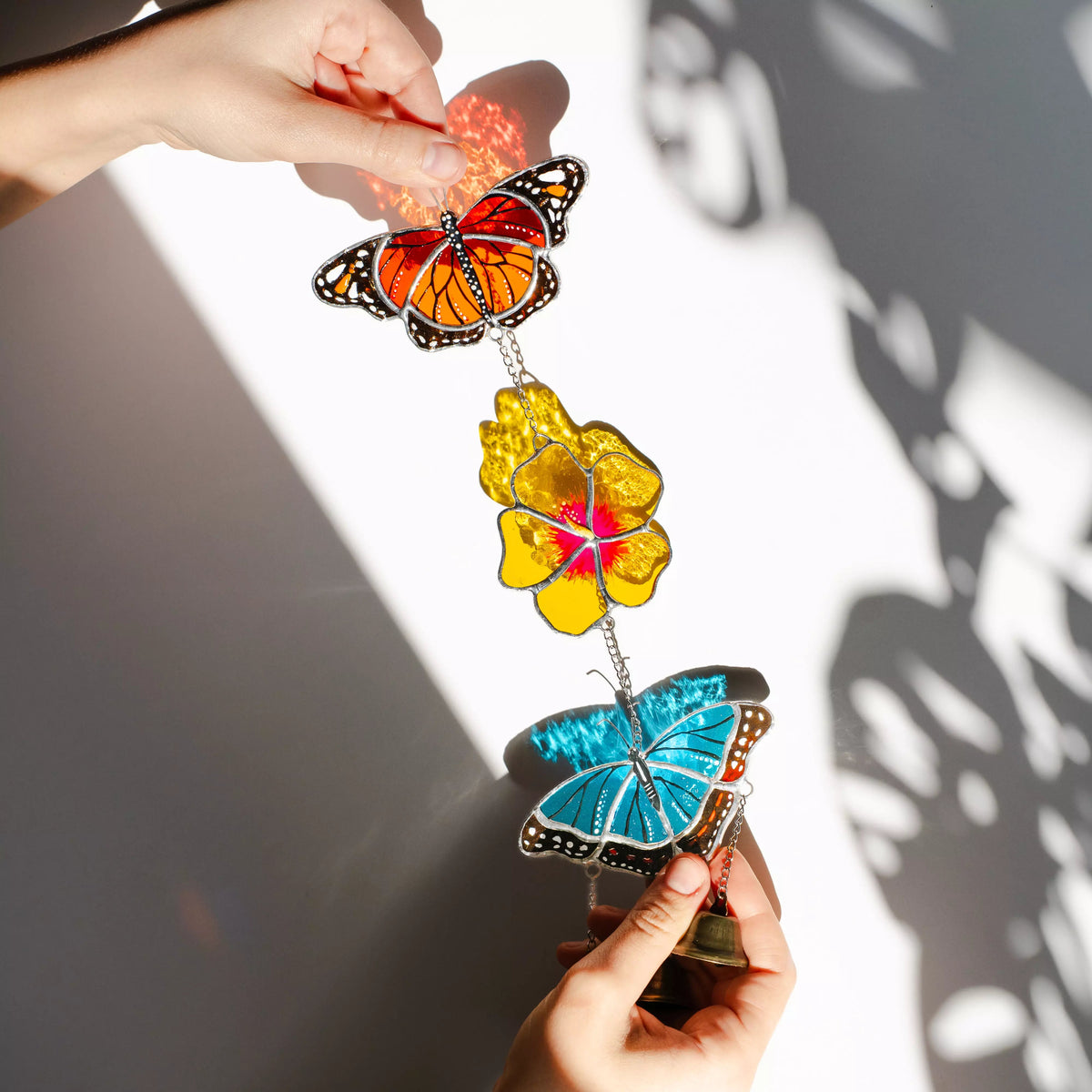 Stained glass butterfly and flower ornament held by a hand against a white background