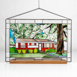 A stained glass window hanging featuring a red house