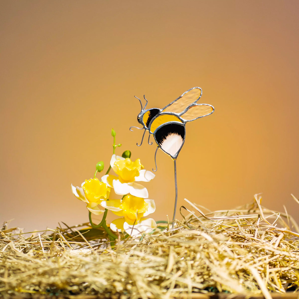 Stained glass bee plant stake on a yellow flower with a warm background
