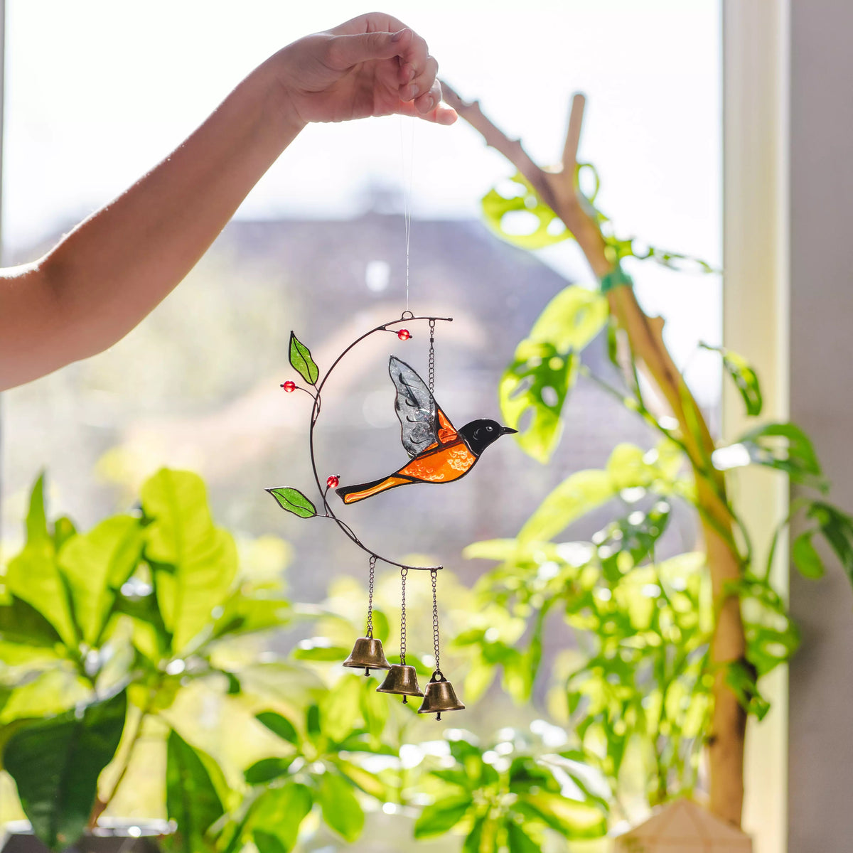 Stained glass bird with bells hanging by a hand against a blurred greenery background