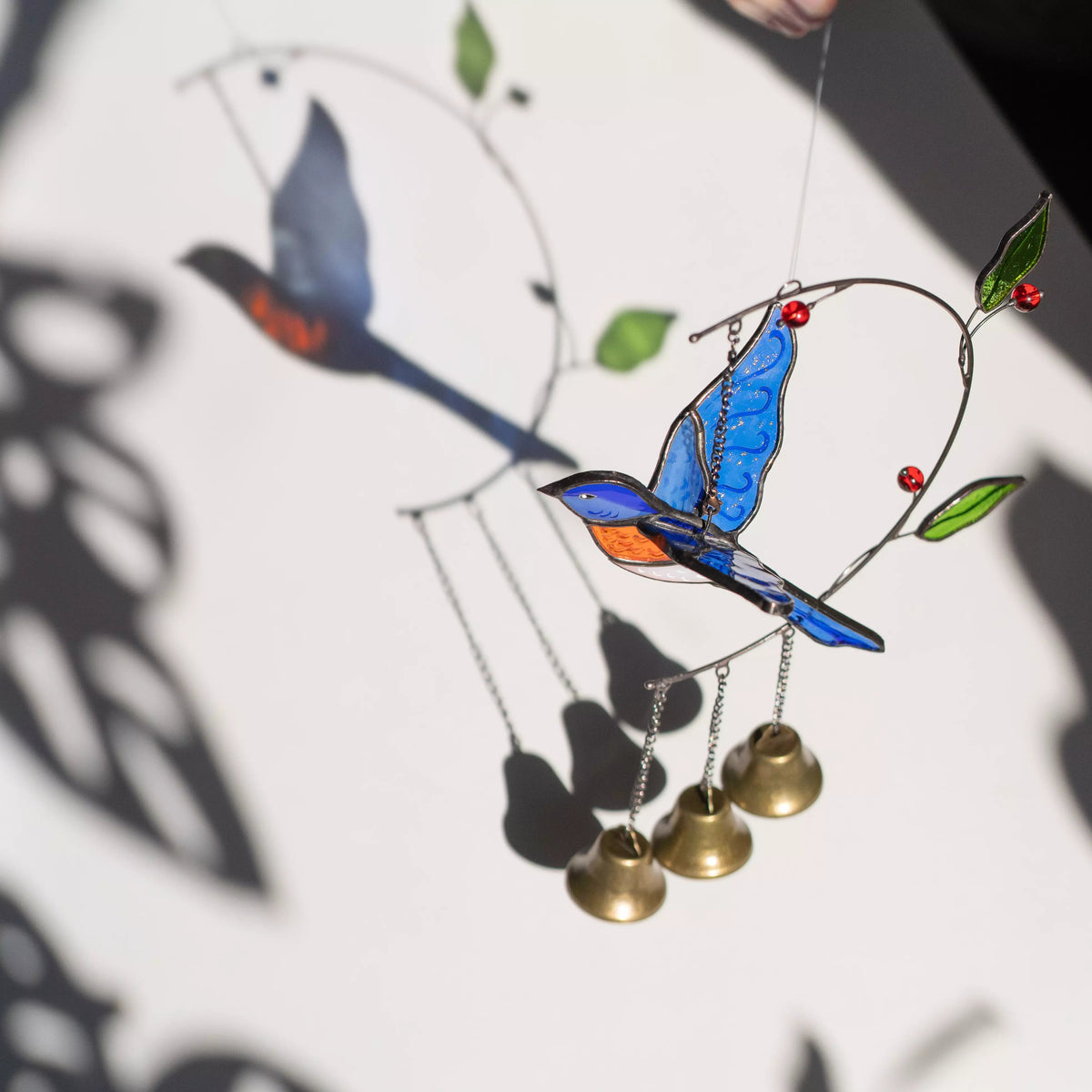 Stained glass bluebird with bells on a white background casting a colorful shadow